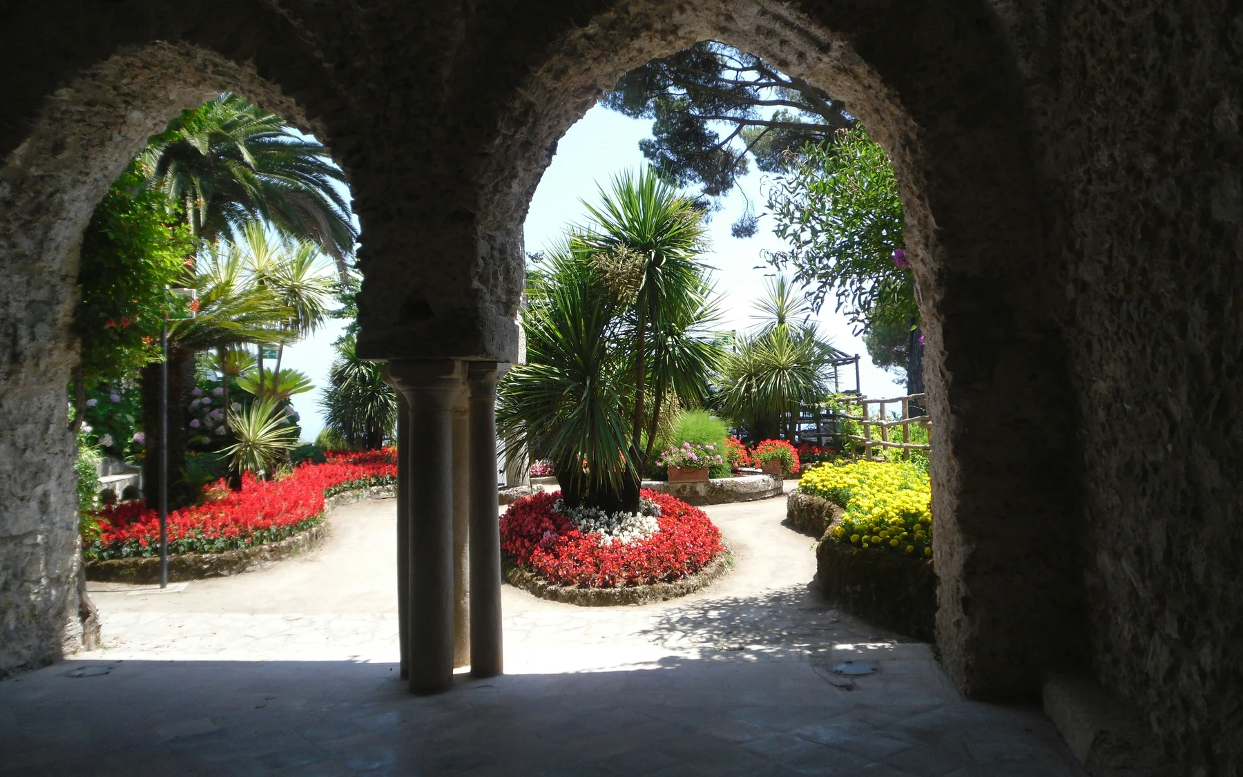 Flower beds and palms seen through stone arches at Villa Rufolo in Ravello