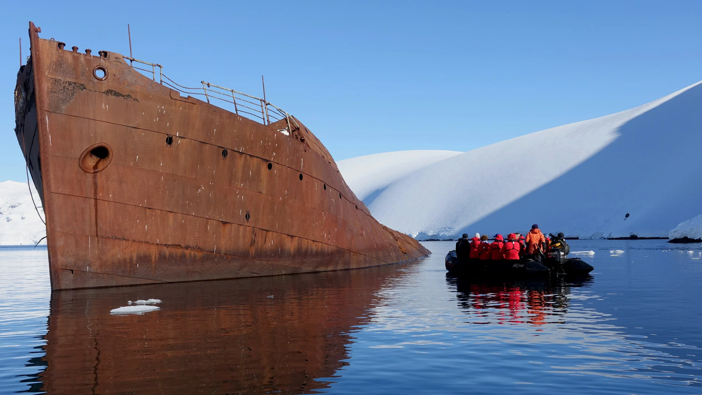 Zodiac visitors beside a rusted shipwreck and snowy Antarctic shoreline