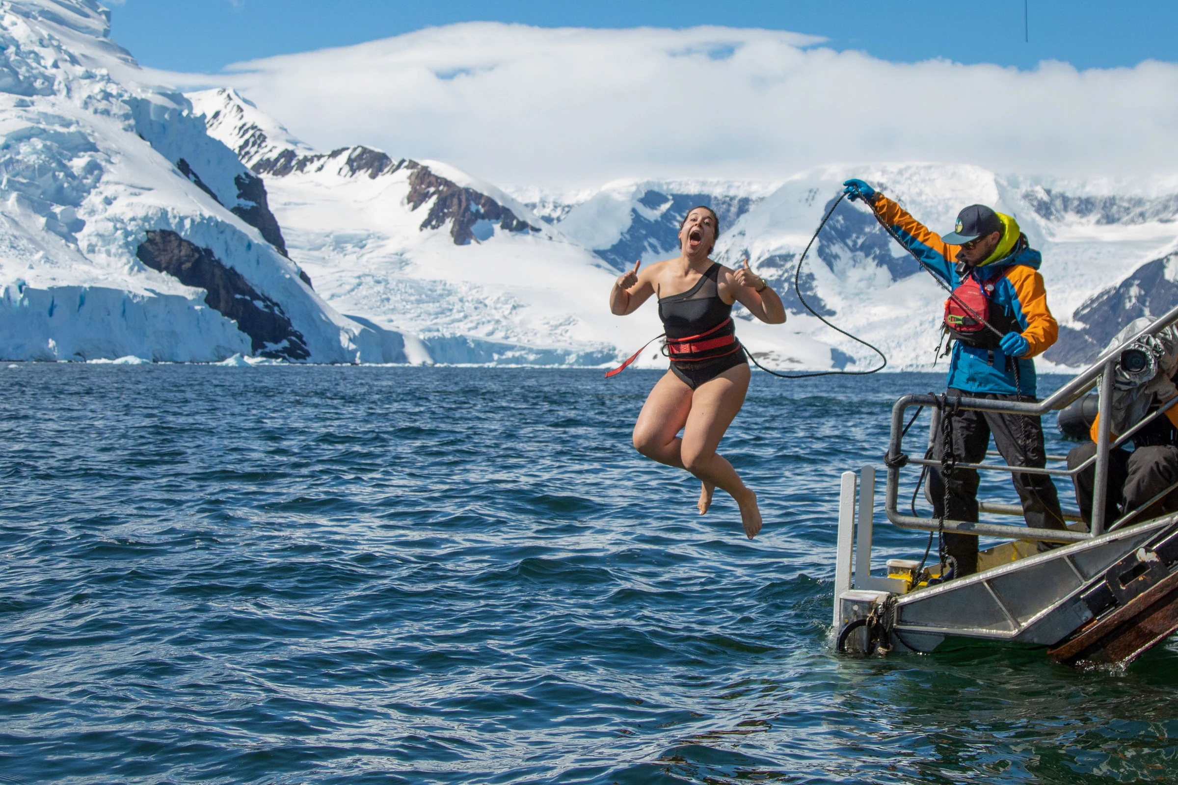 A tethered polar plunge beside an expedition vessel and snowy mountains