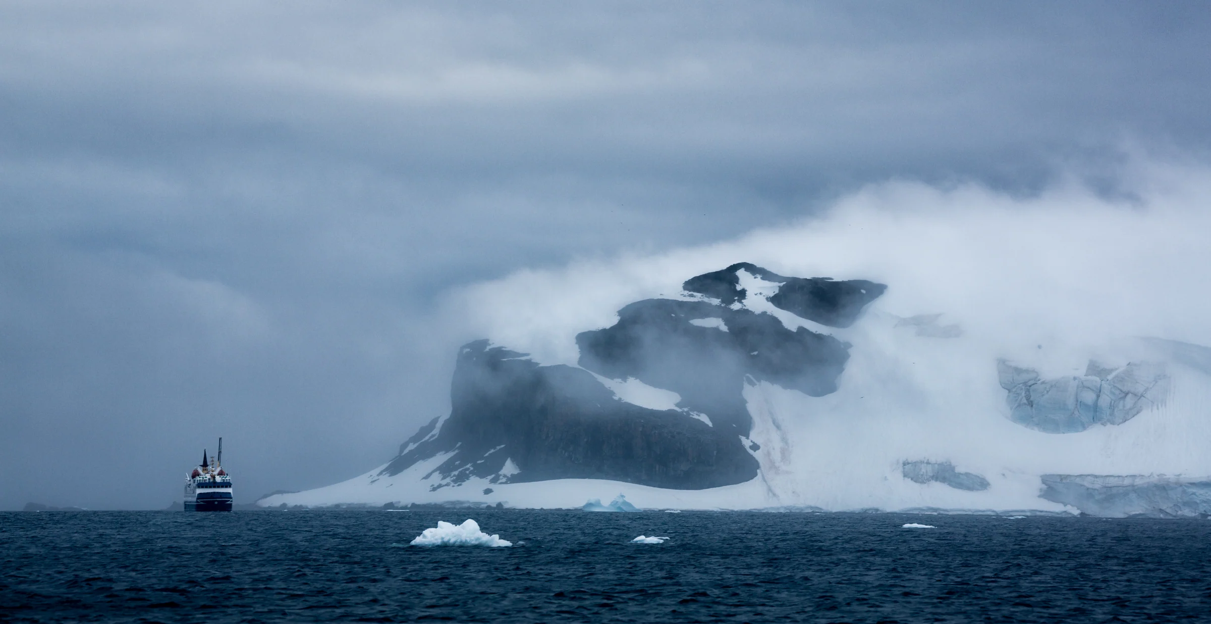 Expedition ship beside a misty, snow-covered Antarctic coastline