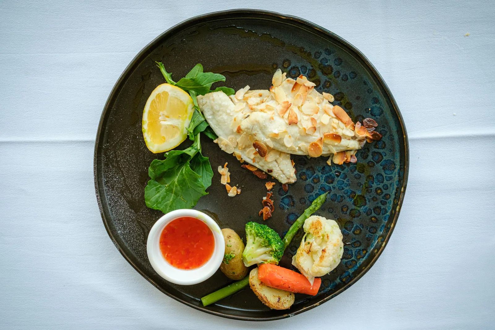 A plated dish with vegetables, lemon and a small bowl of sauce