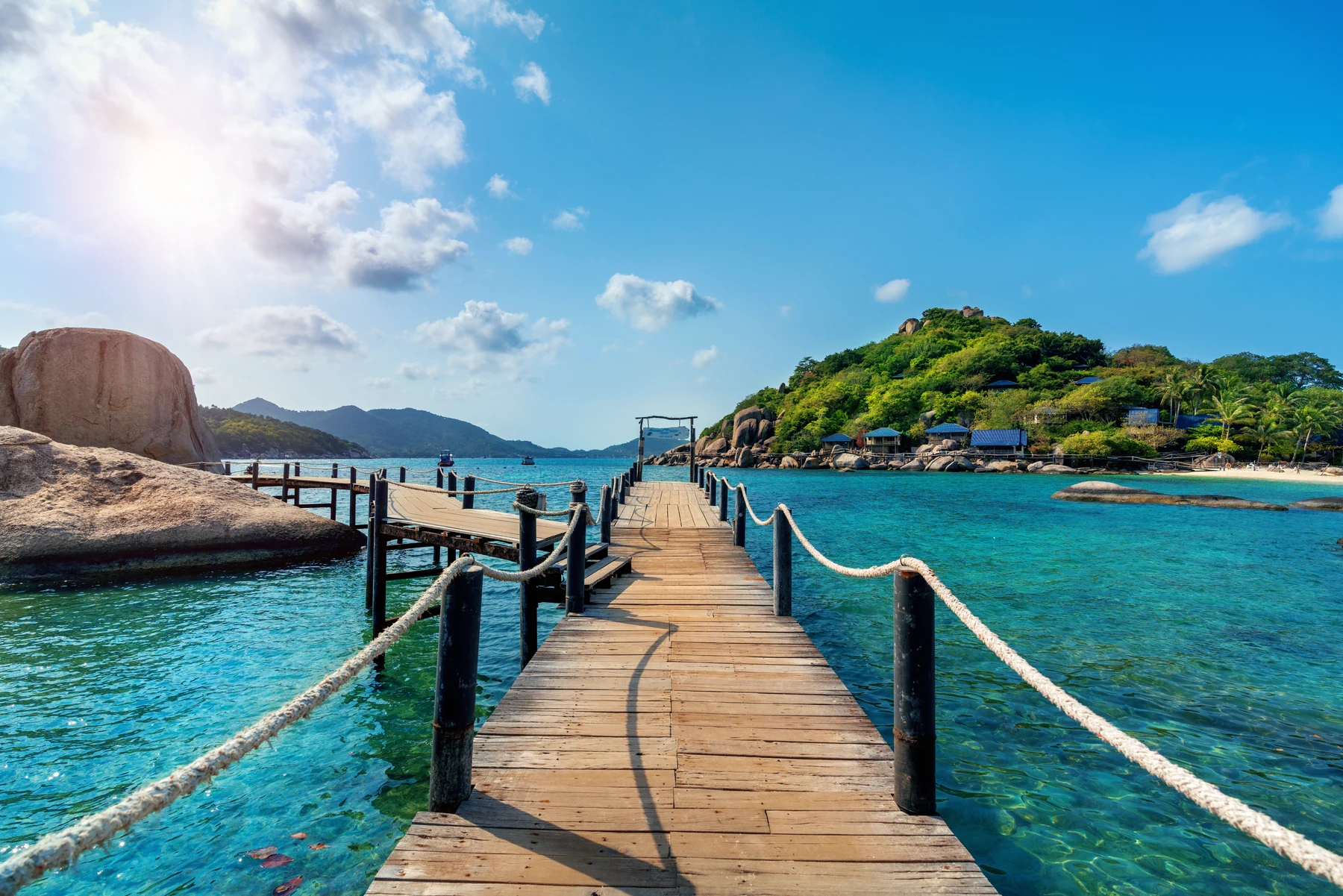 A wooden walkway curving around coastal rocks beside clear turquoise water and green islands