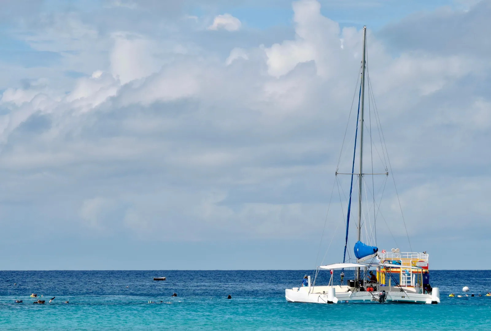 A catamaran anchored beside swimmers in clear turquoise water