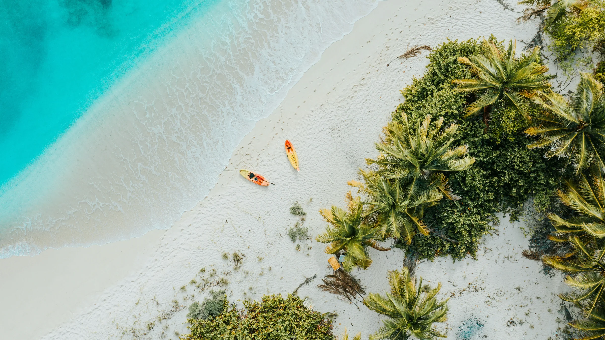 Two kayaks on a pale sandy beach between turquoise water and palm trees