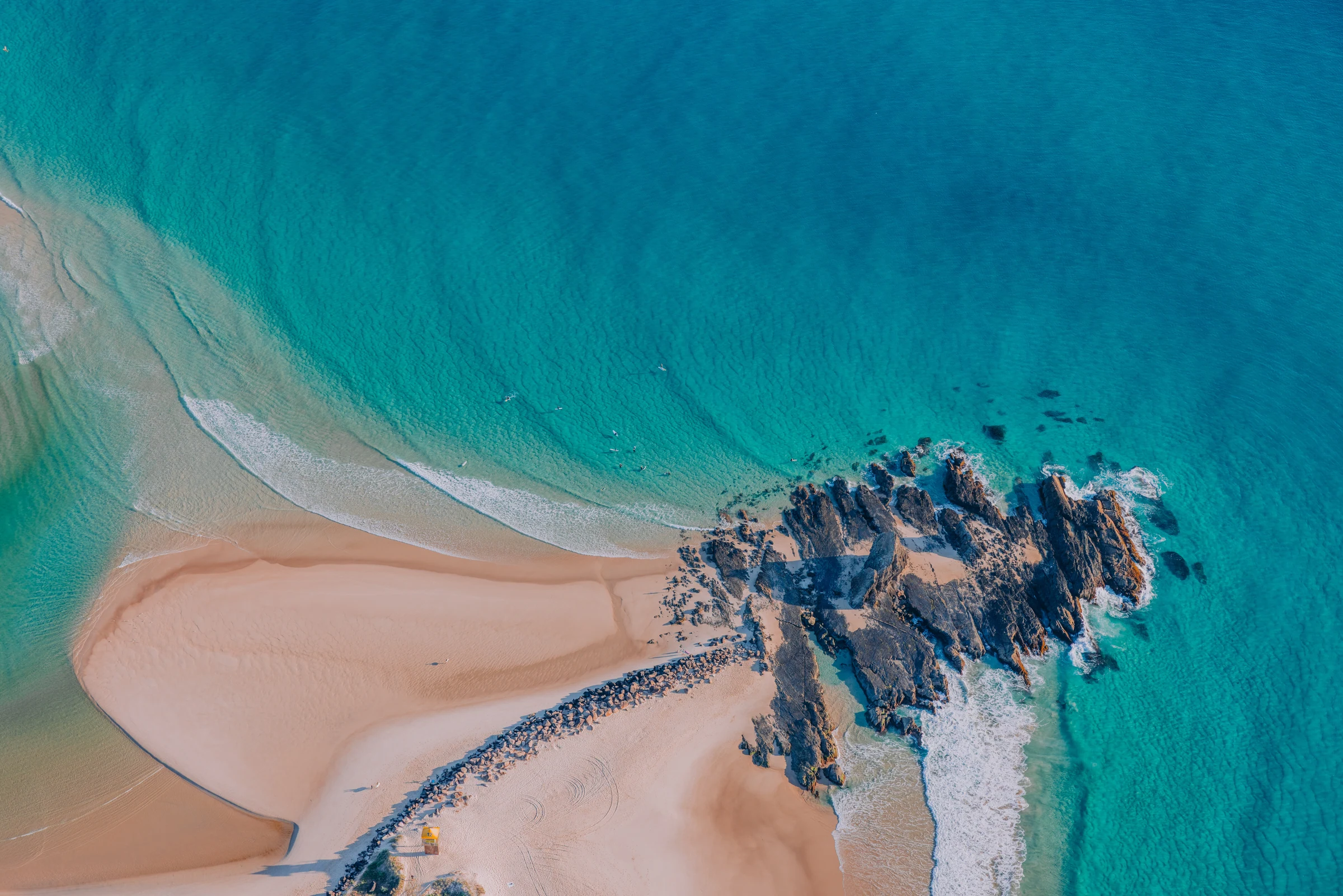 Aerial view of turquoise water, a sandy beach and coastal rocks on the Gold Coast