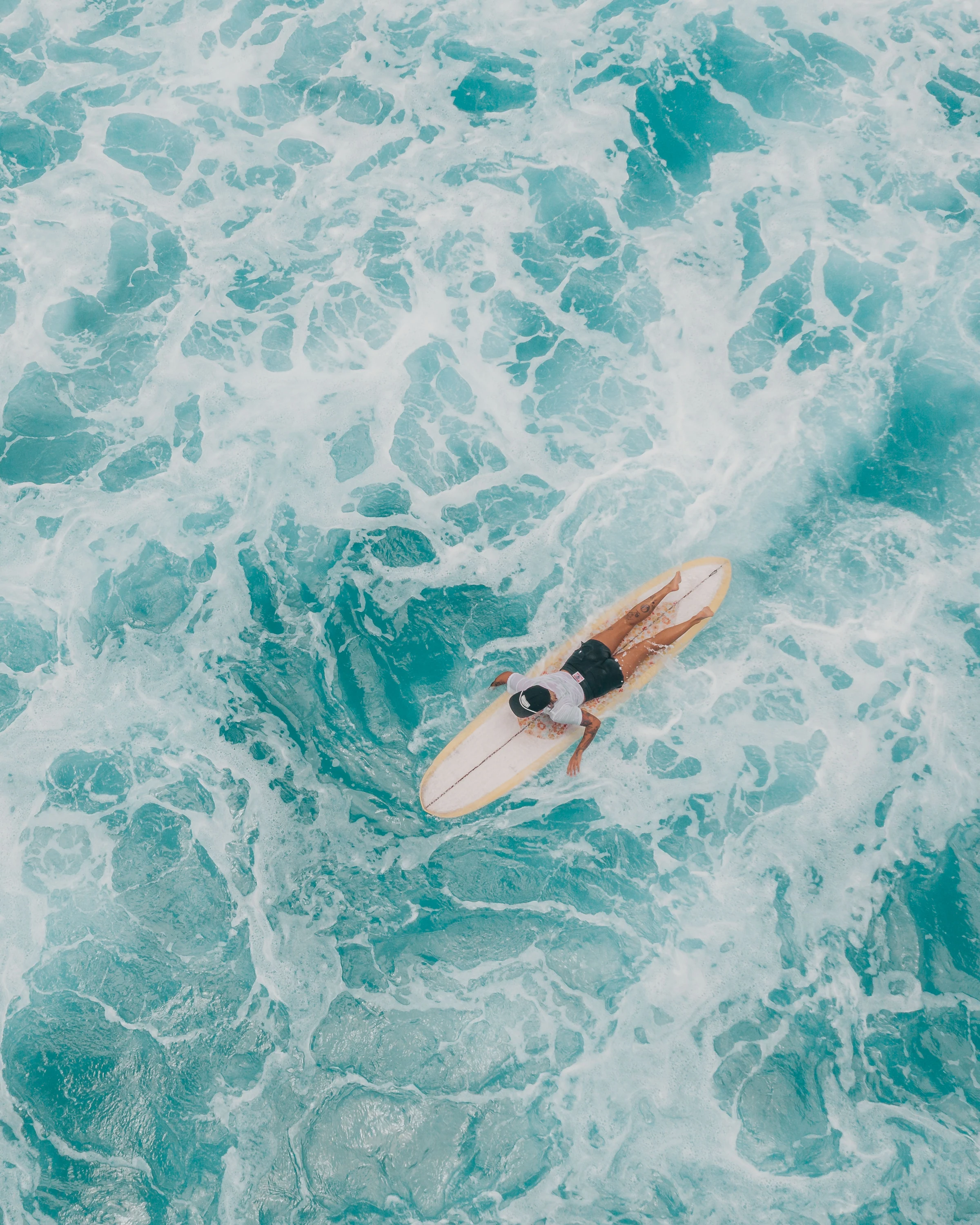 Surfer paddling a surfboard through turquoise water and white surf