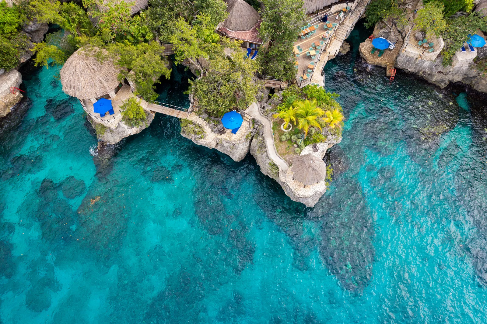 Thatched buildings and stone terraces linked by bridges above clear coastal water