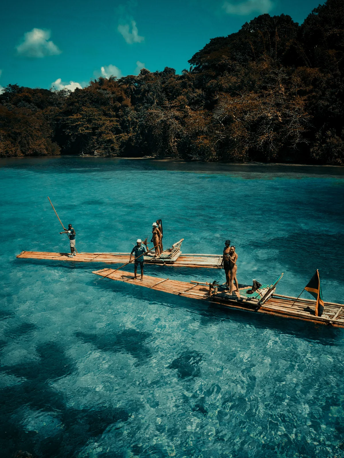 Guides and travelers on bamboo rafts in clear turquoise water