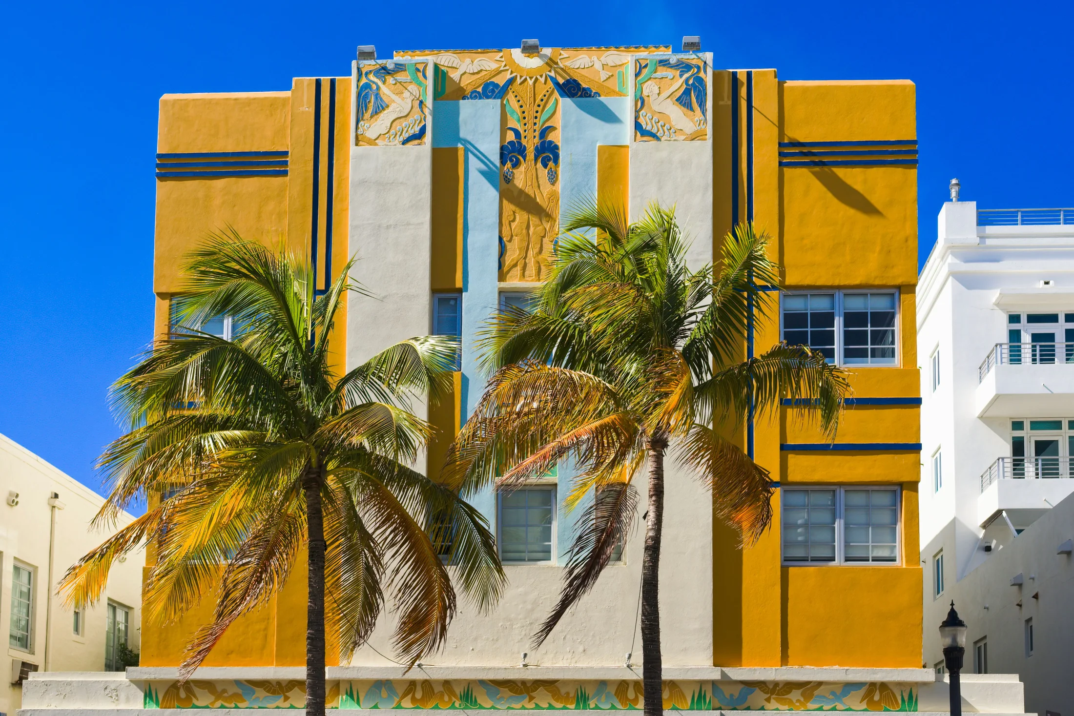 Palm trees in front of a yellow and white Art Deco facade in Miami Beach