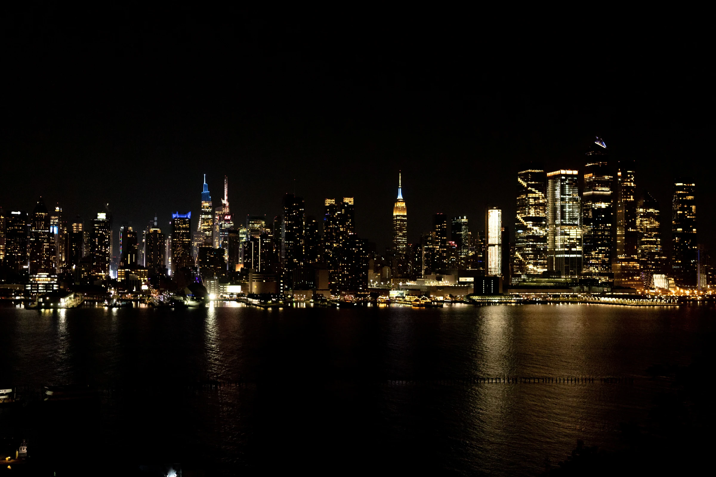 Manhattan skyline at night with the illuminated Empire State Building and Hudson River reflections