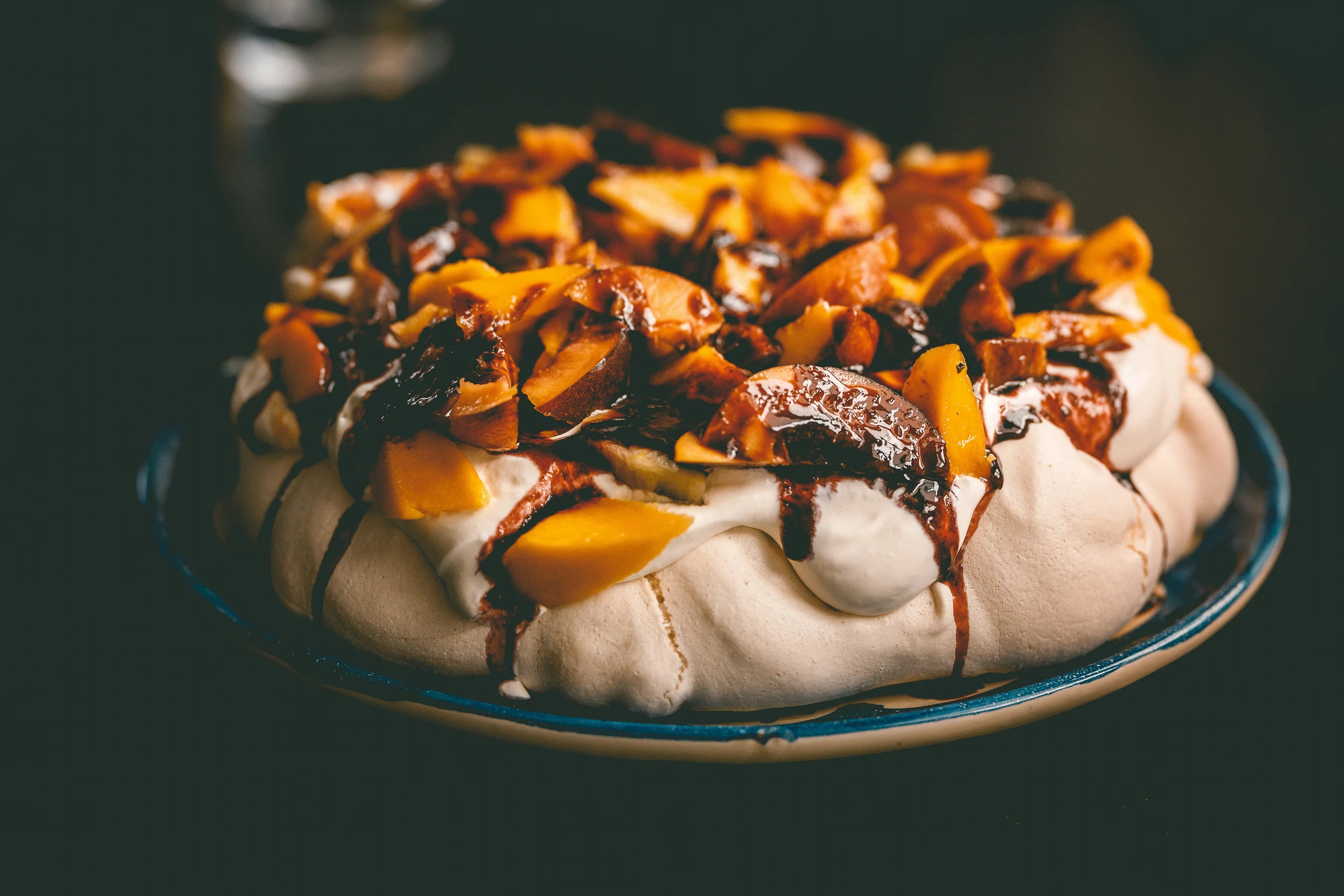 A fruit-topped pavlova with cream and chocolate sauce