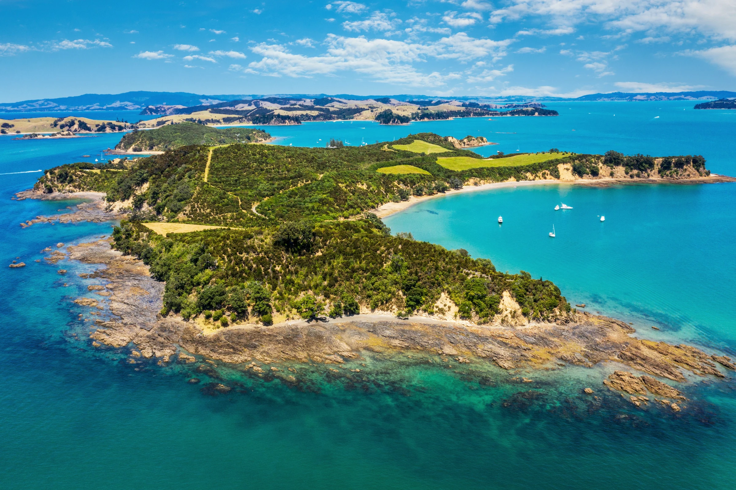 Green coastal hills, sandy coves and anchored sailboats surrounded by blue water