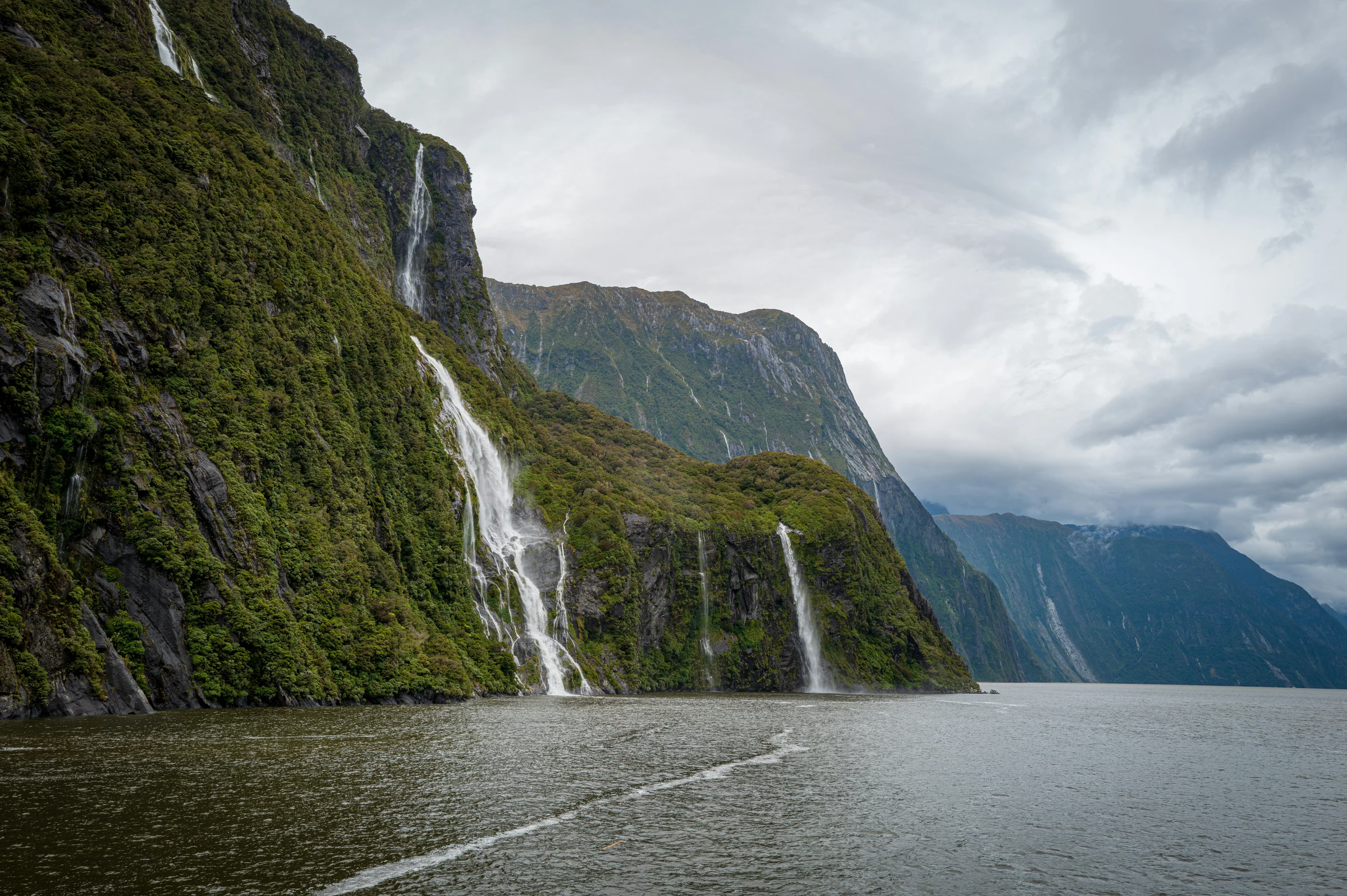 Waterfalls descending green cliffs above the water at Milford Sound