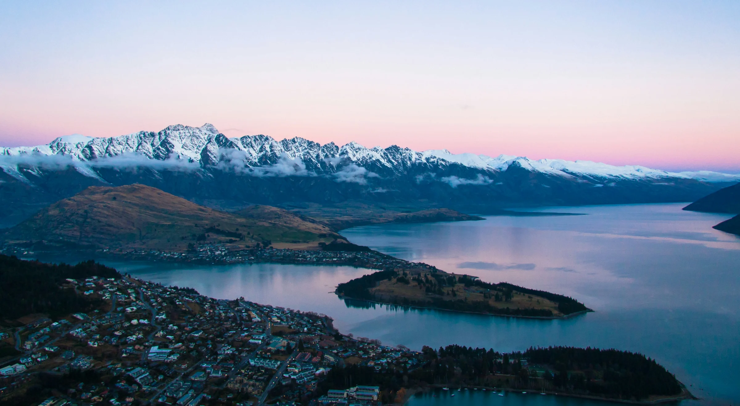 Queenstown and its lake beneath snowy mountains and a pink evening sky