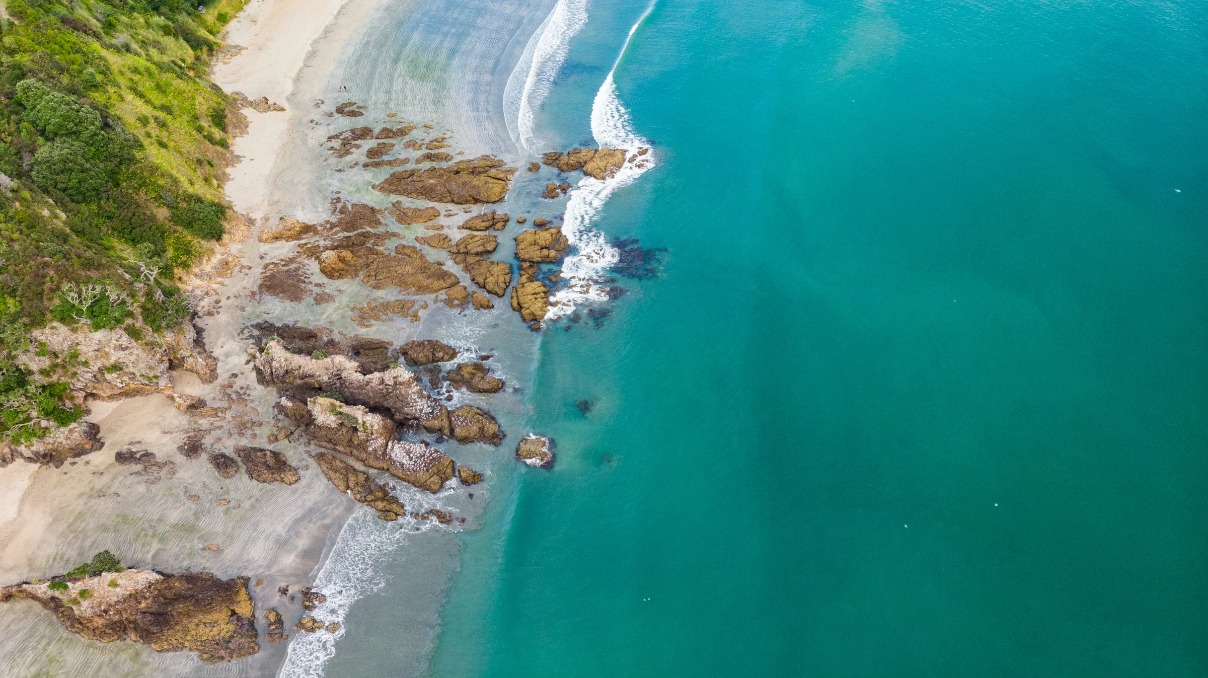 An aerial view of a rocky Waiheke shoreline beside clear turquoise water