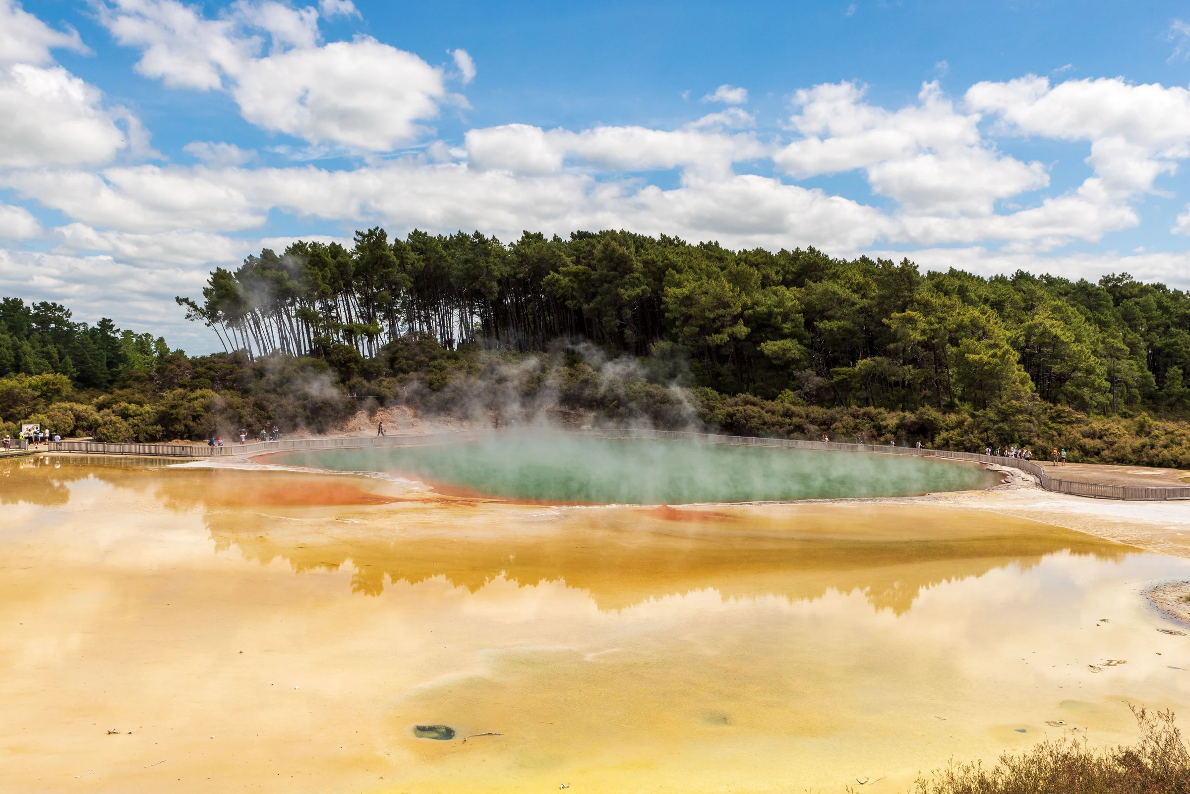 Steaming geothermal pool with an orange mineral rim and surrounding boardwalk