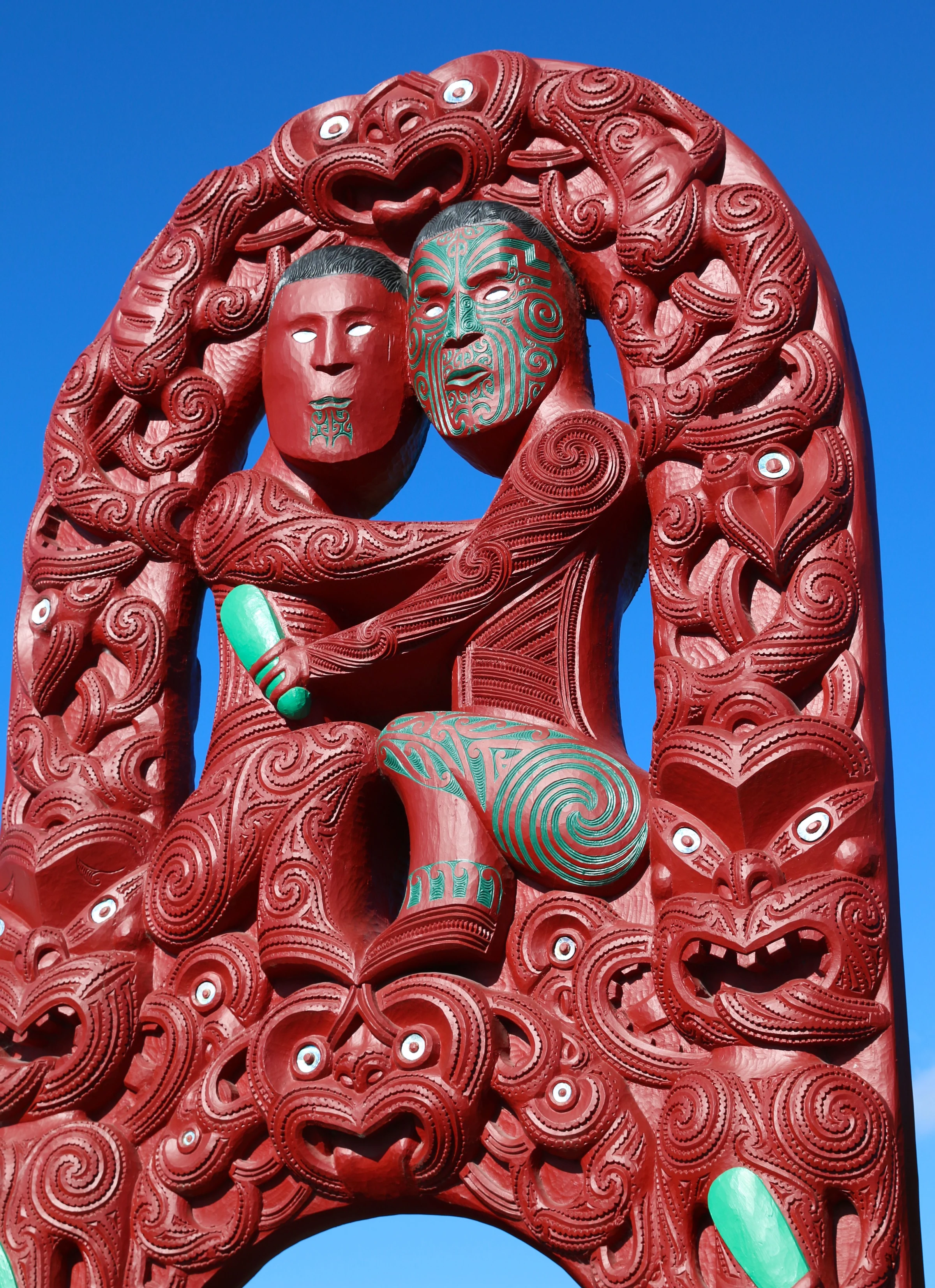 Red and green Māori carving against a blue sky