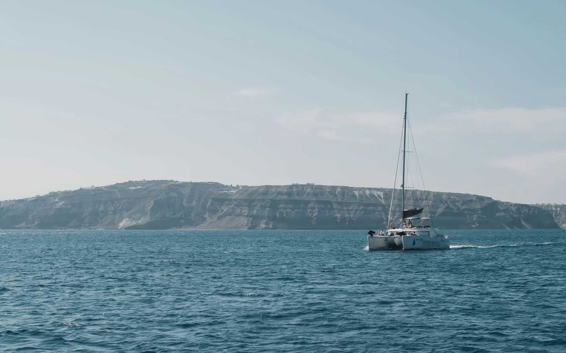 A catamaran on blue water beneath Santorini’s volcanic cliffs
