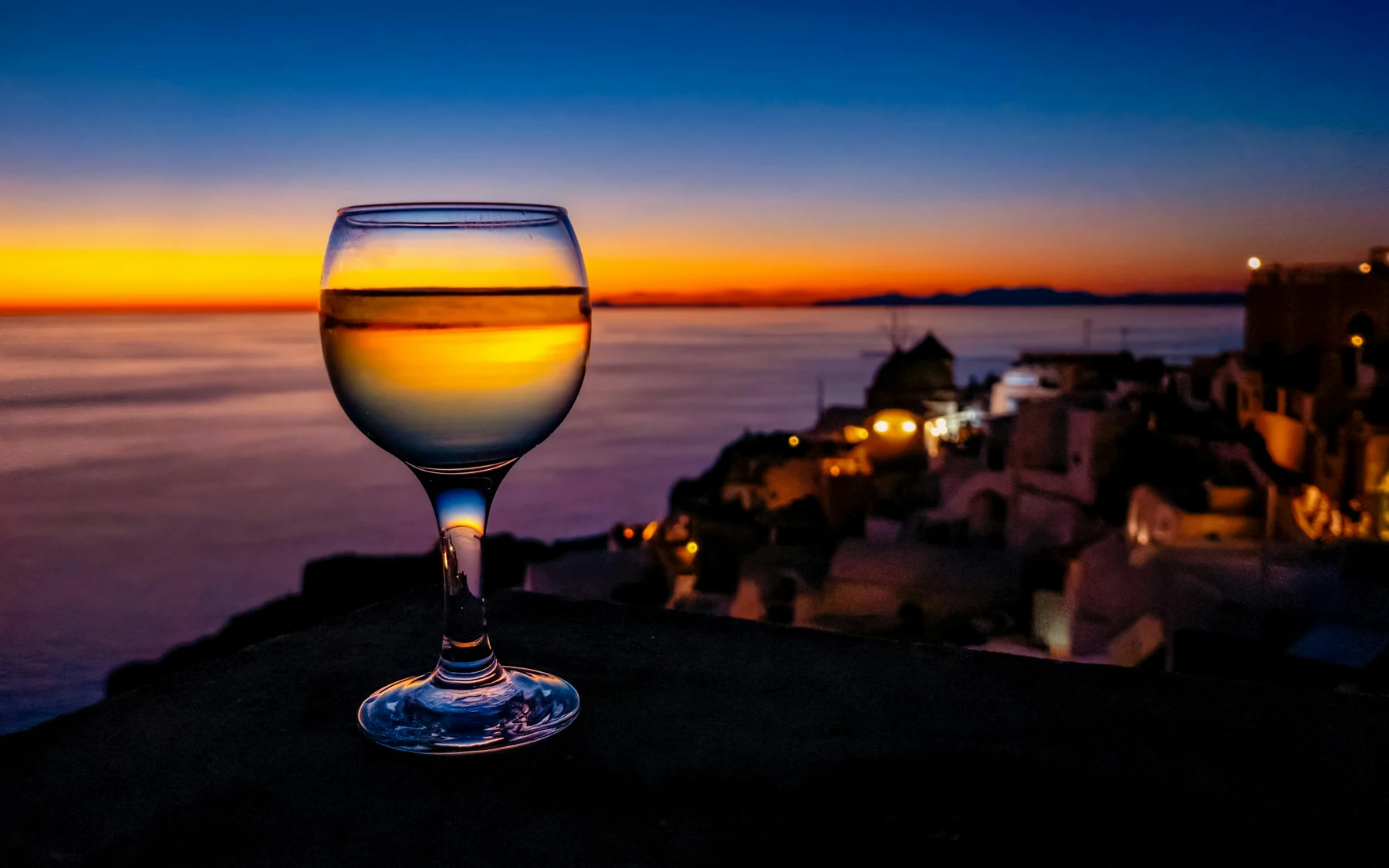 A glass of white wine overlooking Santorini’s coast at sunset