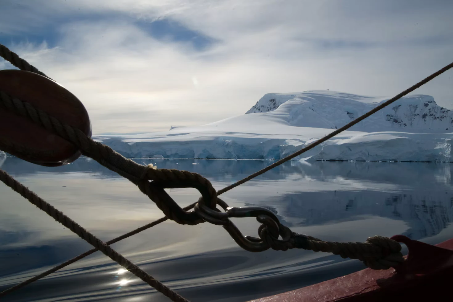 Snow-covered coastal cliffs seen past a sailing vessel’s rigging