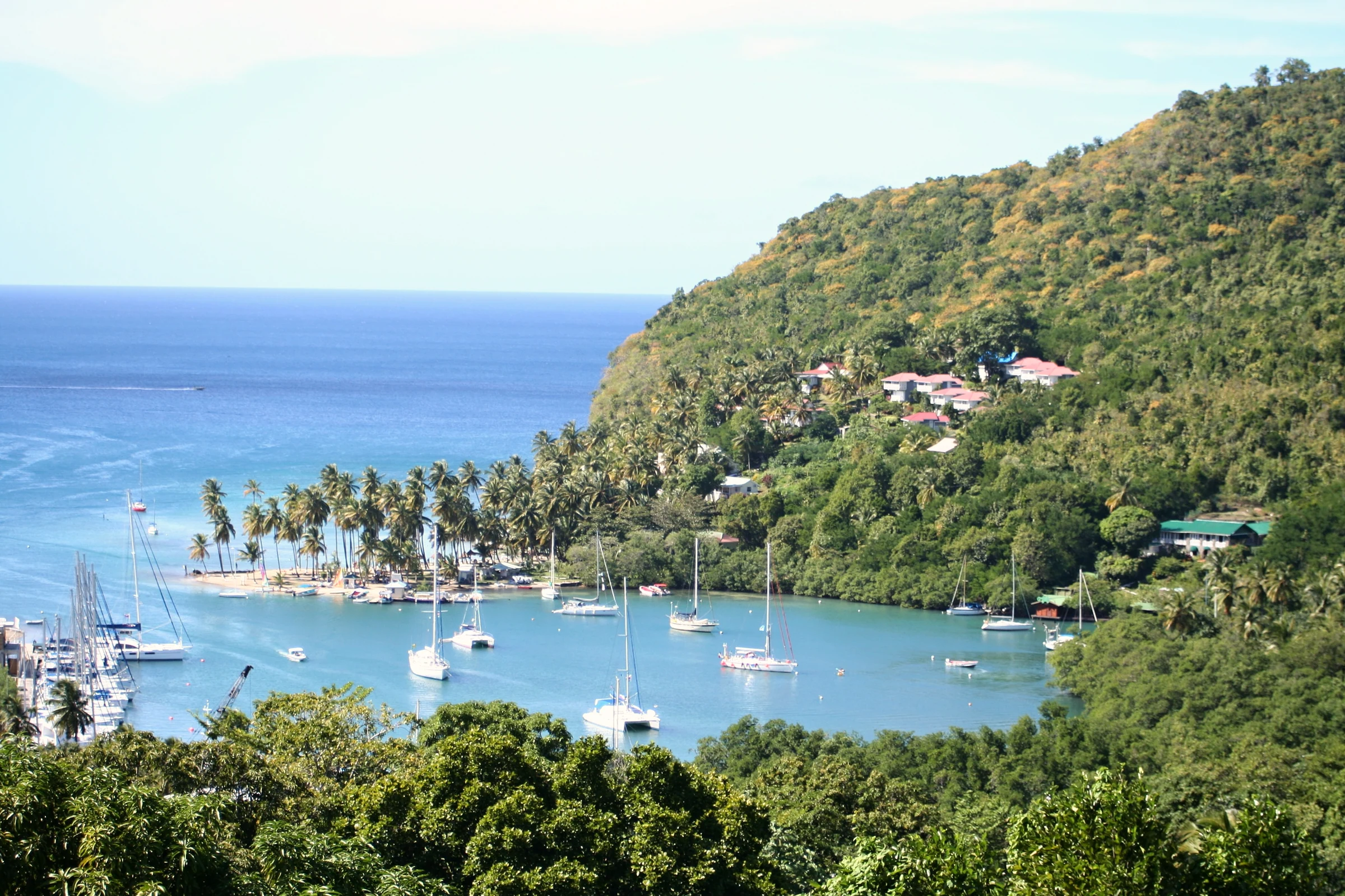Sailboats anchored in a sheltered bay beneath a green hillside and colorful roofs