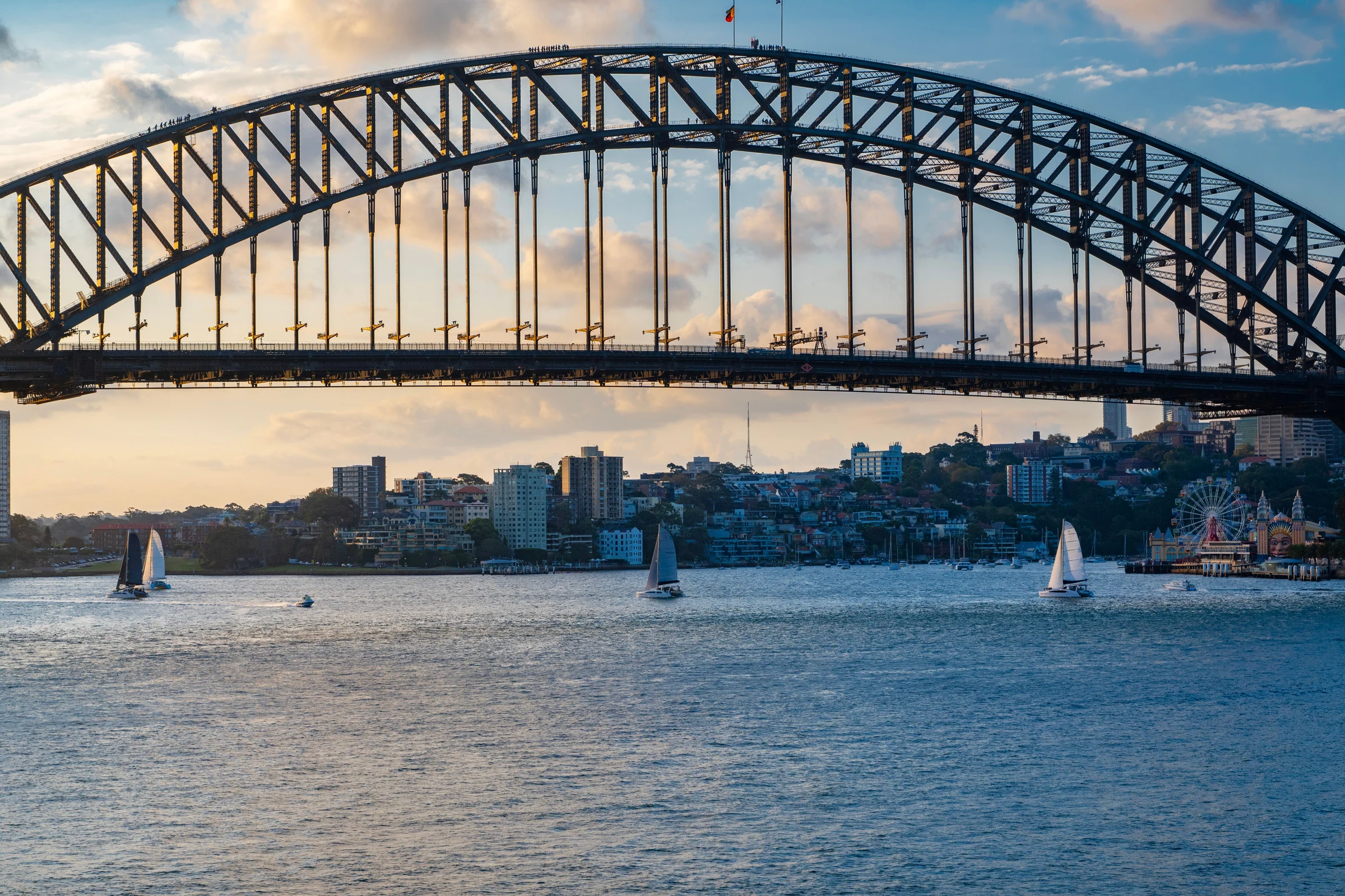 Sailboats beneath Sydney Harbour Bridge in soft evening light