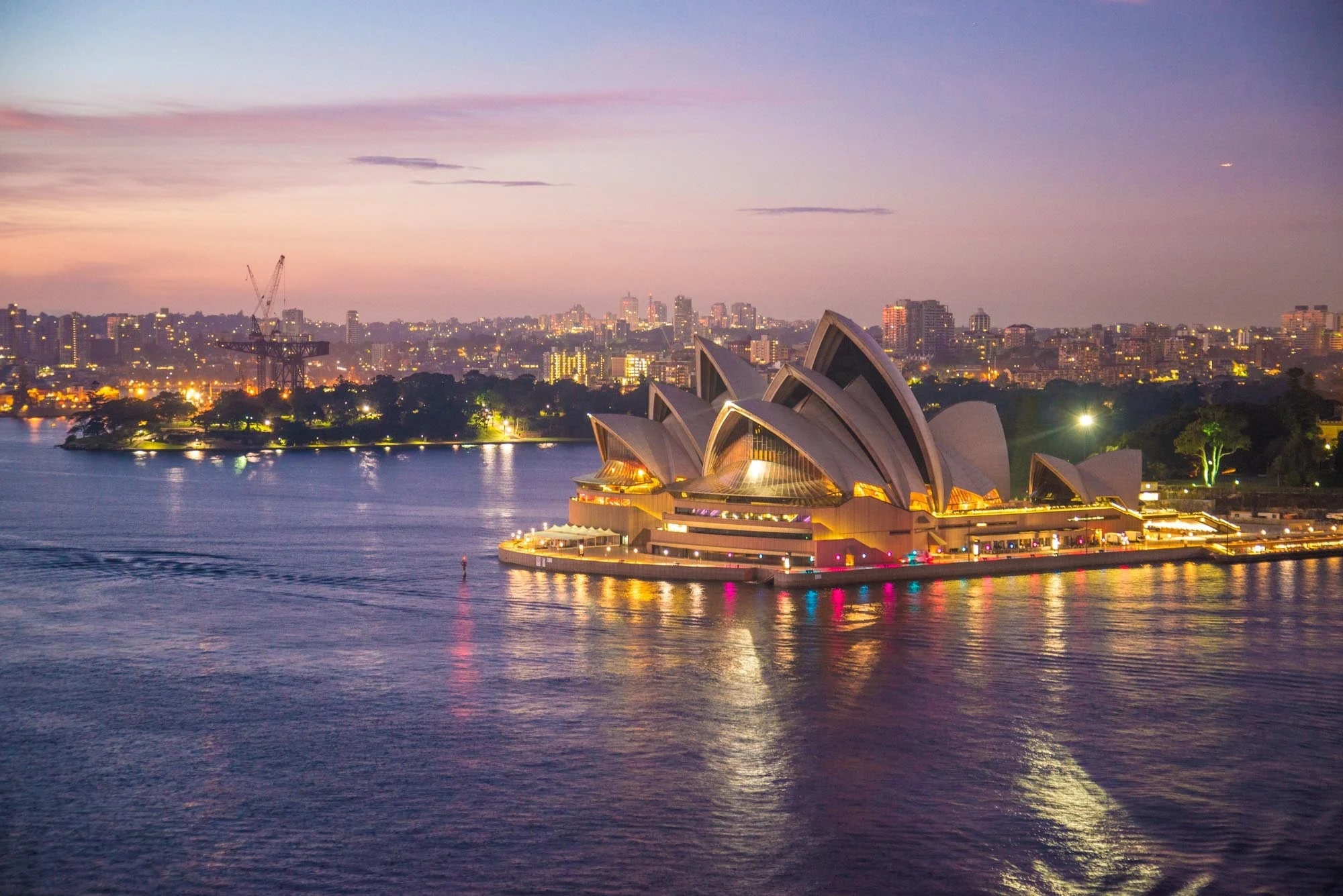 Sydney Opera House illuminated at dusk beside the harbor