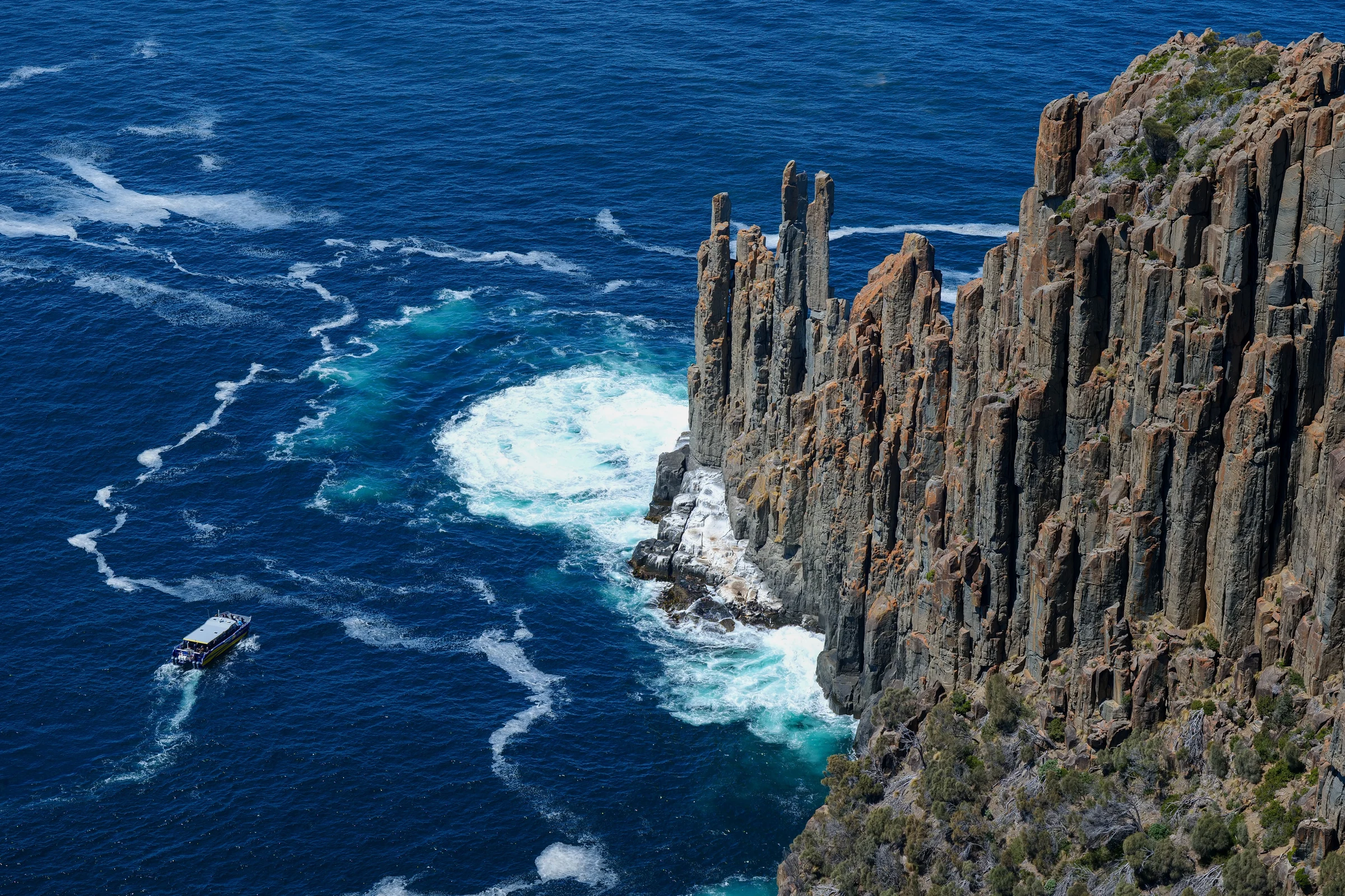 A small tour boat beside towering coastal cliffs in Tasmania