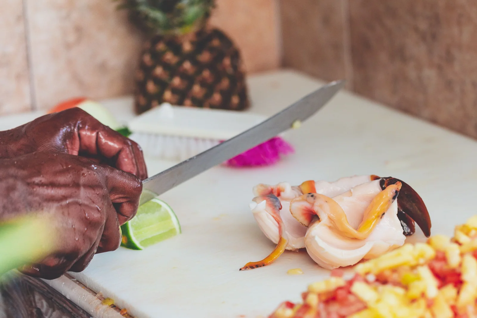Fresh conch, lime and chopped ingredients on a cutting board beside a cook's hands