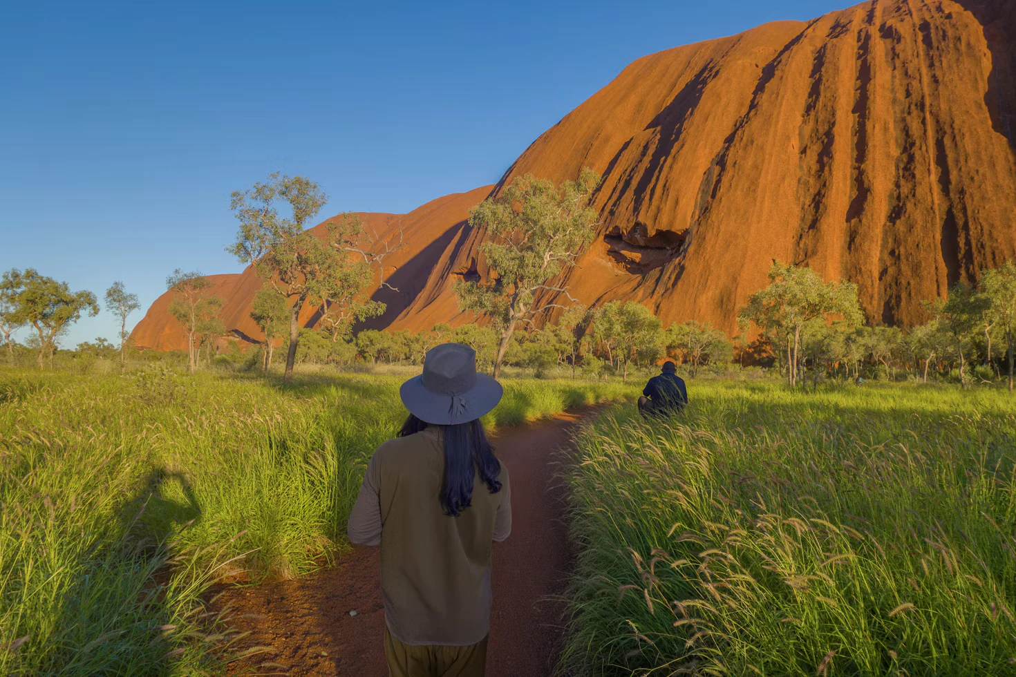 Walkers following a path beside the red rock walls at the base of Uluru