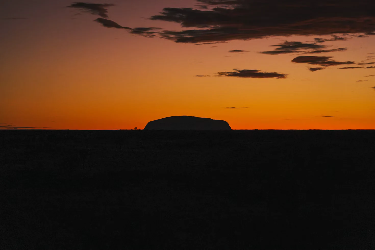 Uluru silhouetted against an orange sunrise sky