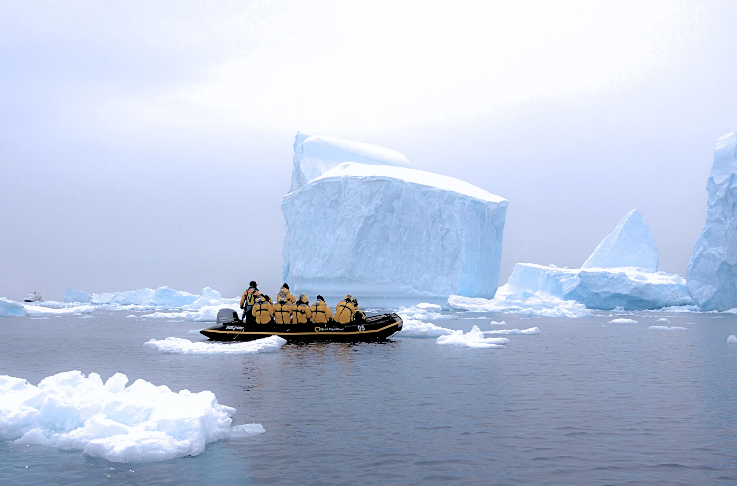 Expedition guests in a Zodiac among large blue-white icebergs