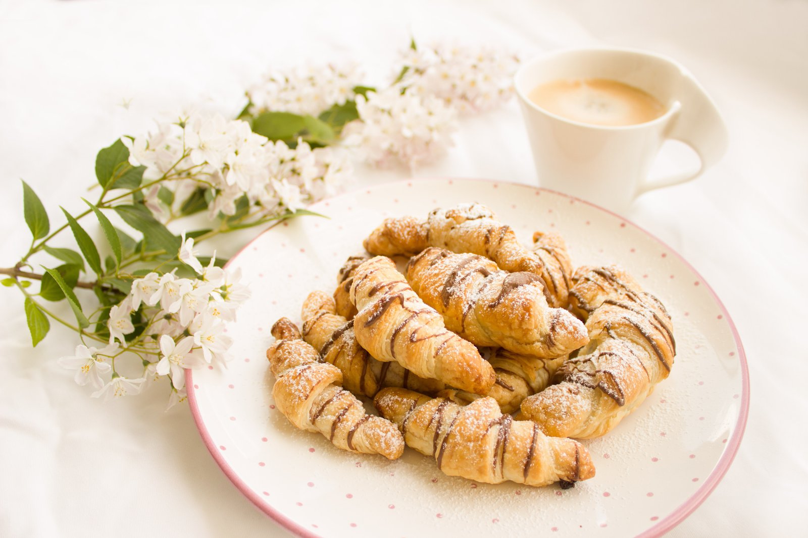 A plate of croissants with coffee and white blossoms