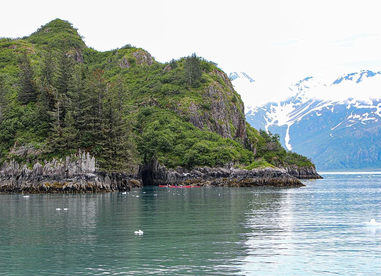 Kayakers beside a rocky forested island in Kenai Fjords National Park