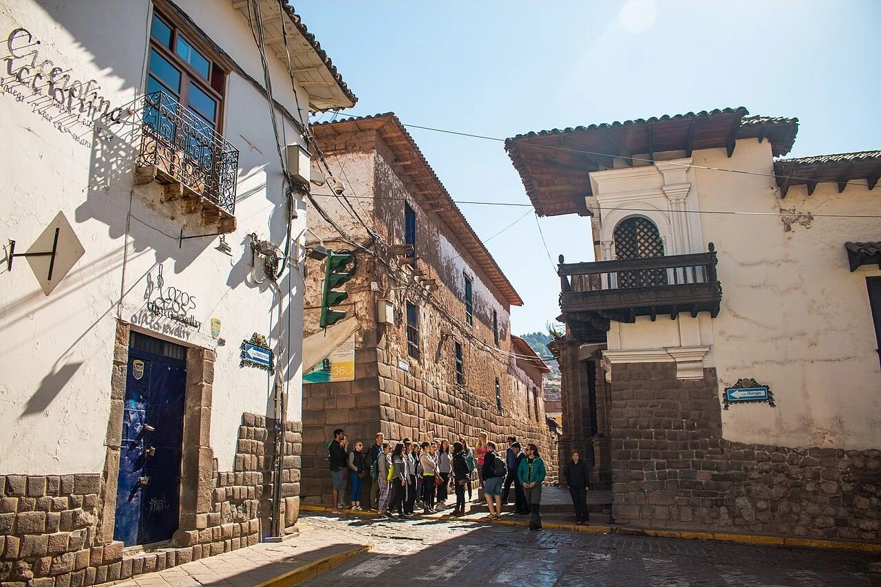 Visitors beside the Inca stone walls and colonial buildings of Calle Hatunrumiyoc in Cusco.