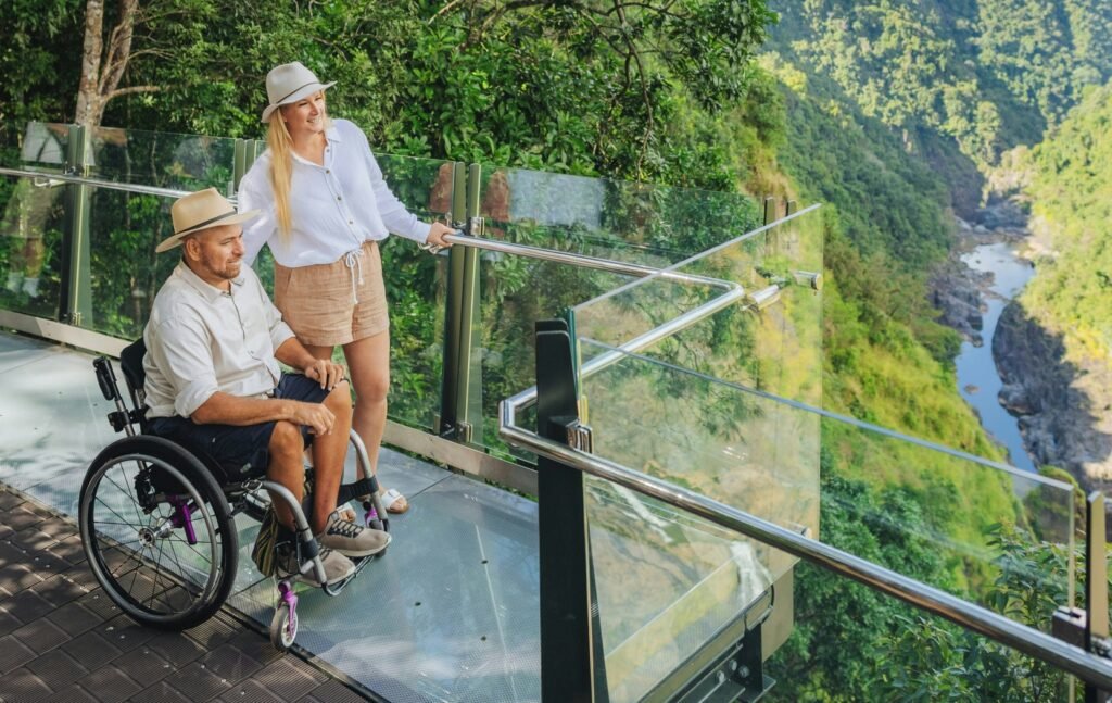 Two travelers, including a wheelchair user, at a forest lookout above a river gorge