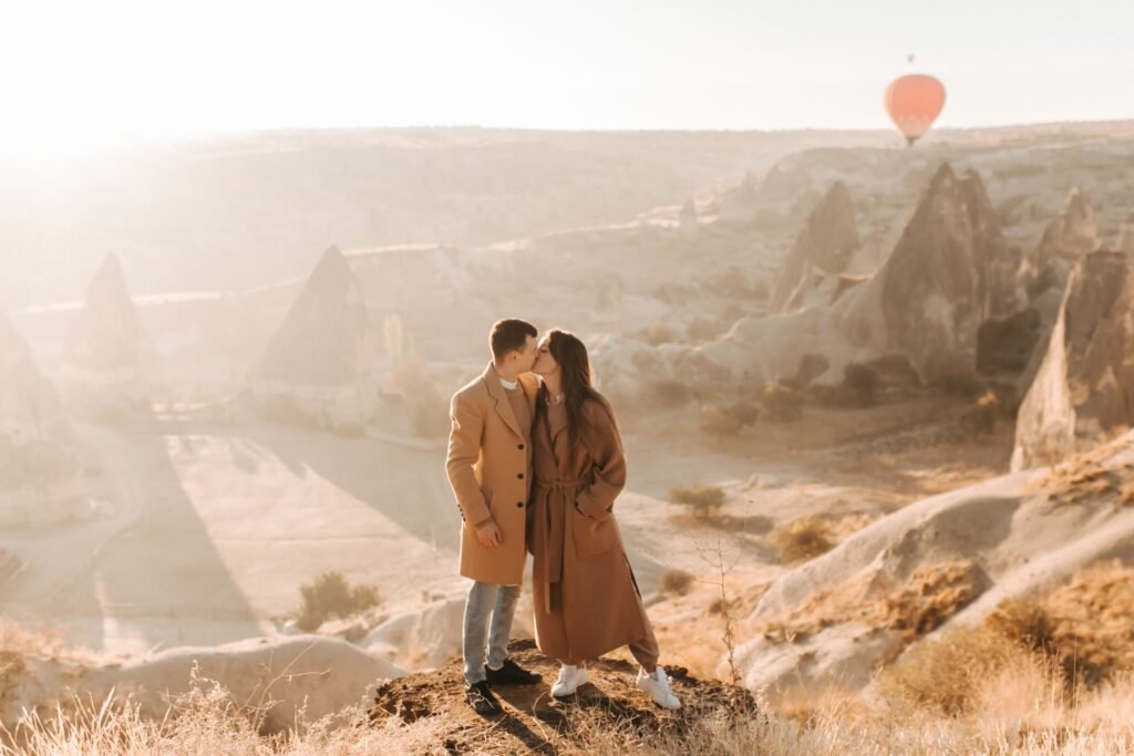 A couple kissing above a rocky valley with a hot air balloon in the distance
