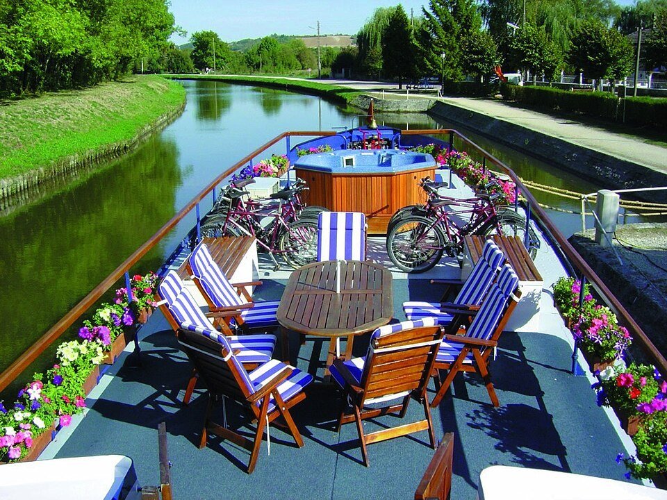 Outdoor dining tables and bicycles on L'Art de Vivre beside a leafy canal