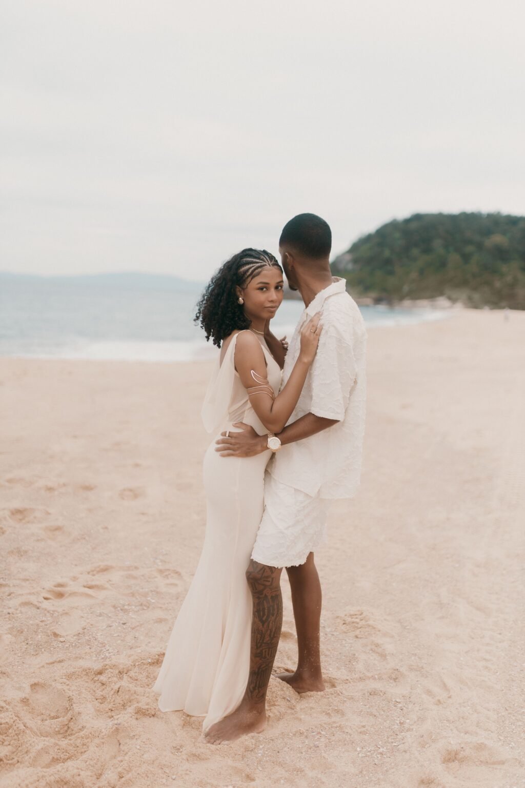 A couple embracing barefoot on a sandy beach beside the sea
