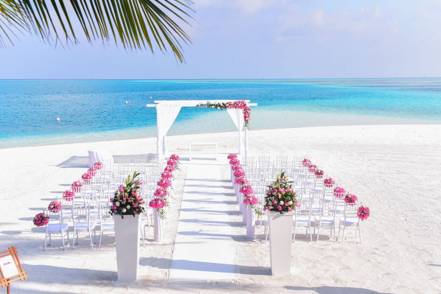 White chairs and a flower-decorated wedding arch beside turquoise sea