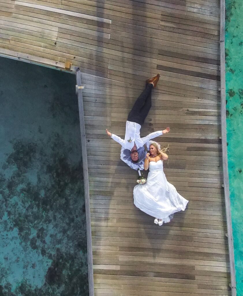 An overhead view of newlyweds lying together on a wooden dock above clear water