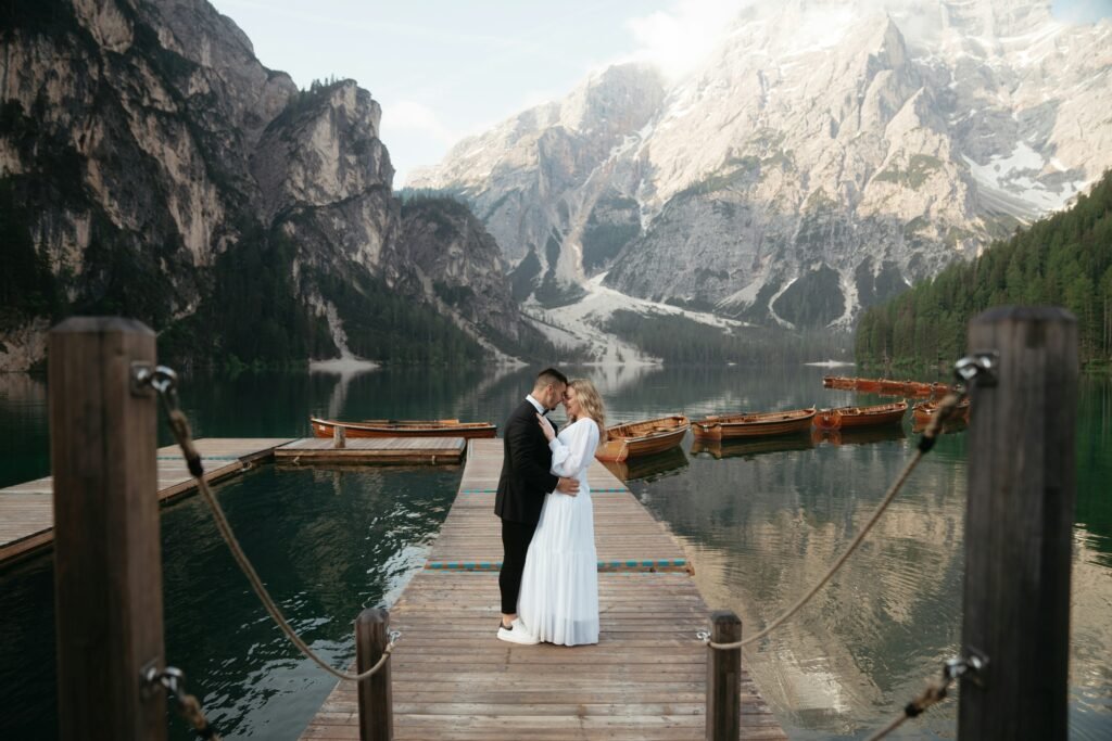 A wedding couple embracing on a wooden dock beside a mountain lake