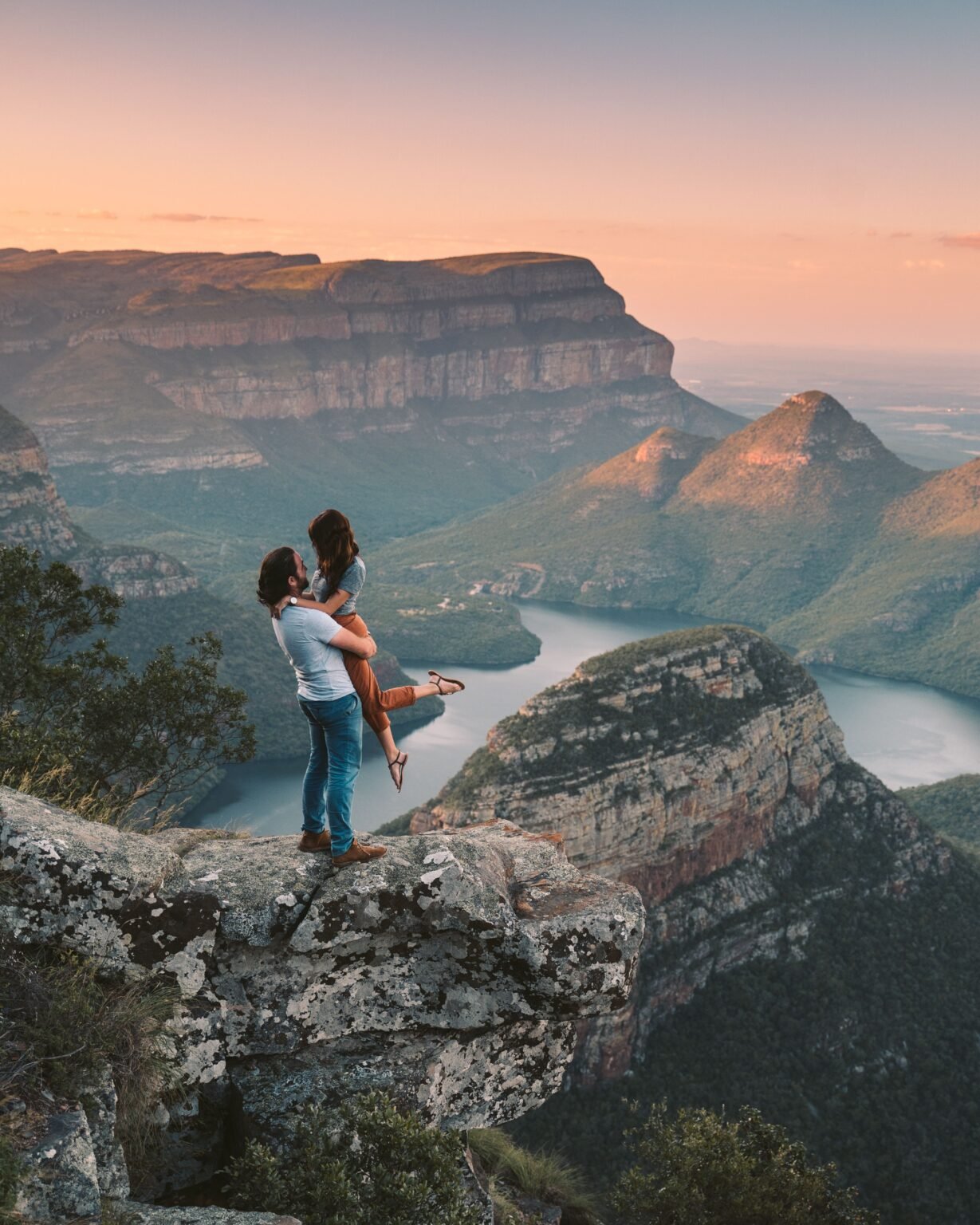 A couple embracing on a rocky overlook above a winding river at sunset