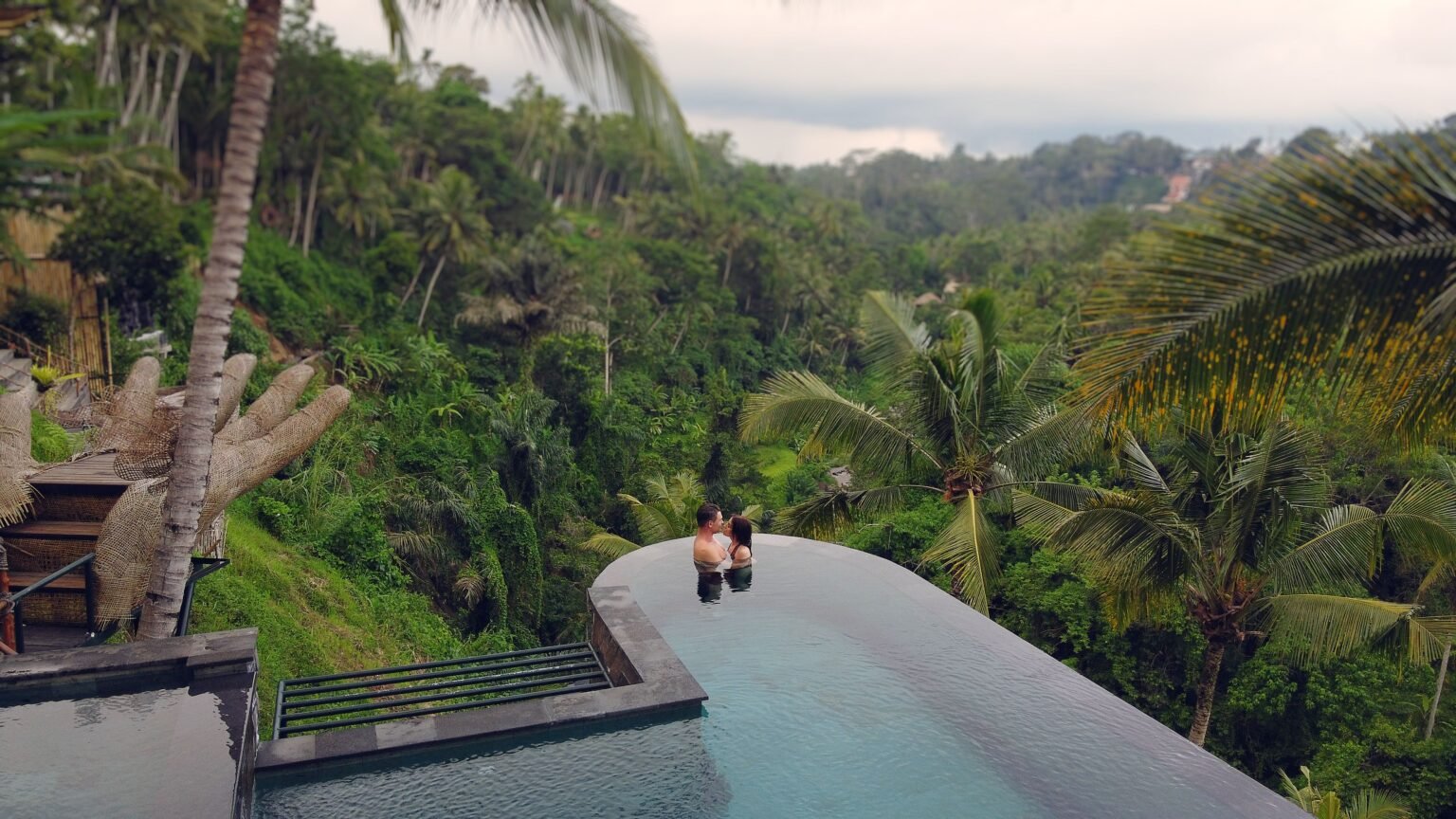 A couple enjoying an infinity pool overlooking a lush tropical valley