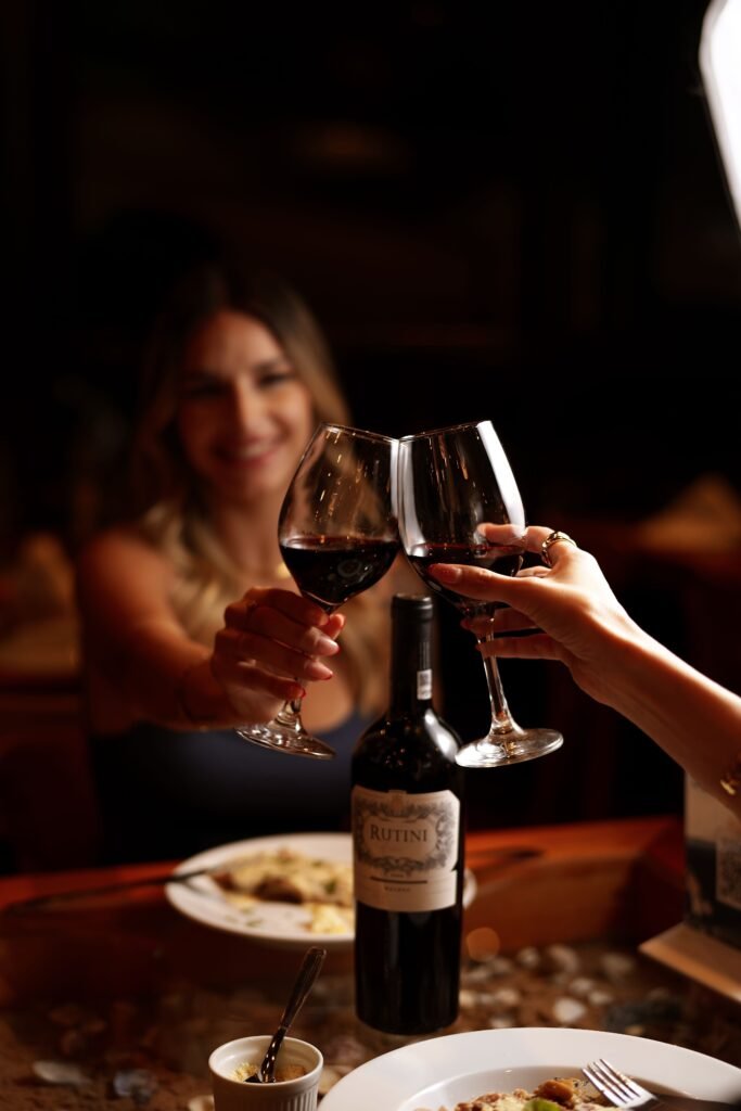 Two people toasting with red wine over dinner, with a wine bottle on the table