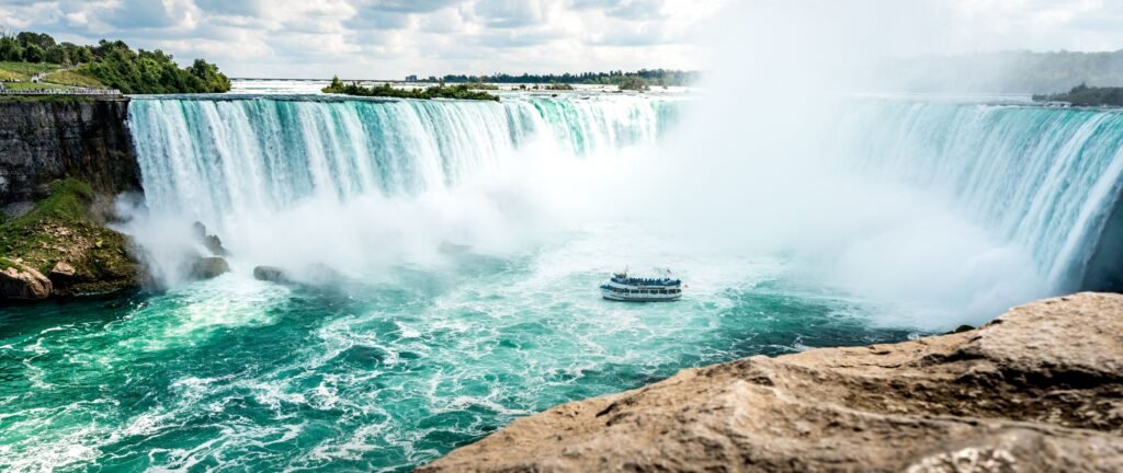 A sightseeing boat beneath Niagara Falls surrounded by turquoise water and mist