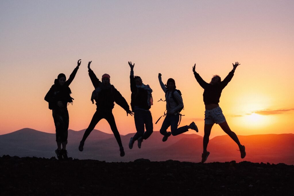 Five friends jumping together against a mountain sunset