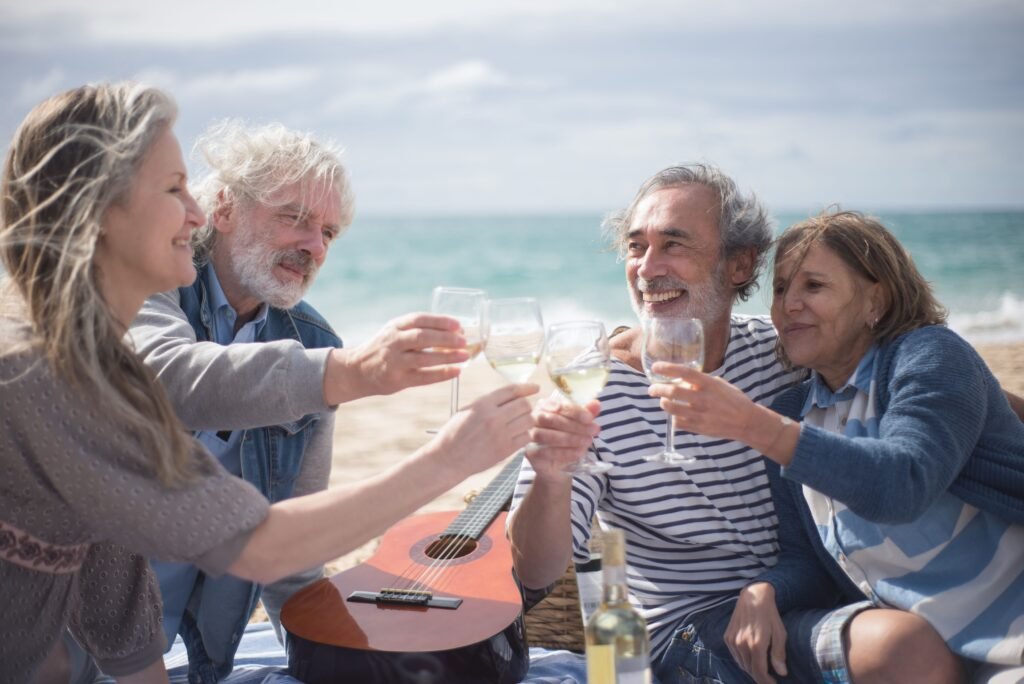 Four friends raising glasses together on a beach beside a guitar